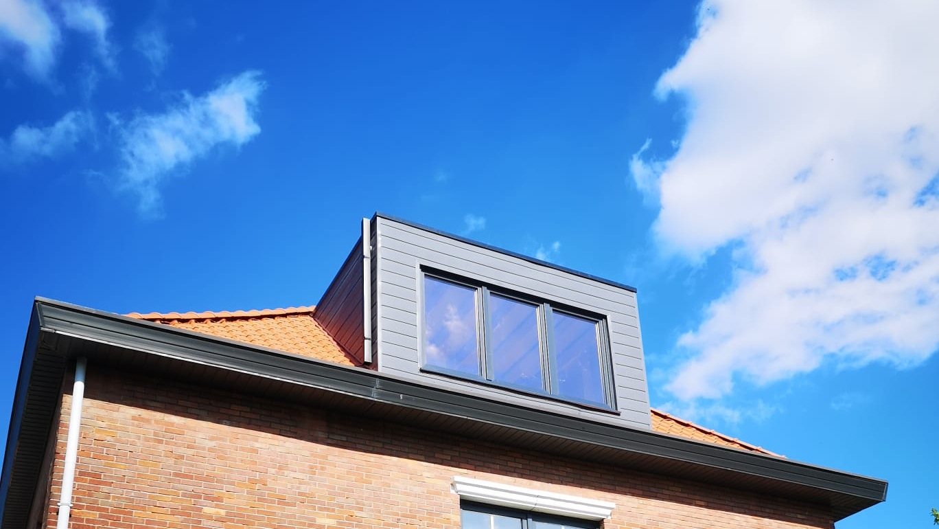 Dakkapel met grijze bekleding op een bakstenen woning